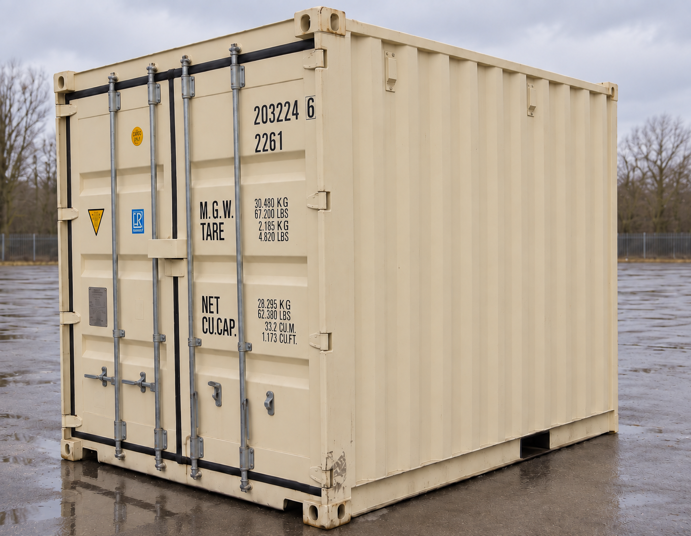 Cream 10-foot standard shipping container at a three-quarter angle showing its double doors, locking bars and cargo rating markings on wet asphalt